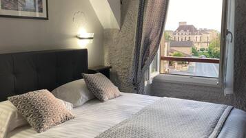 A bedroom with a large bed, a headboard, a nightstand, a wall-mounted light, and a window with curtains.