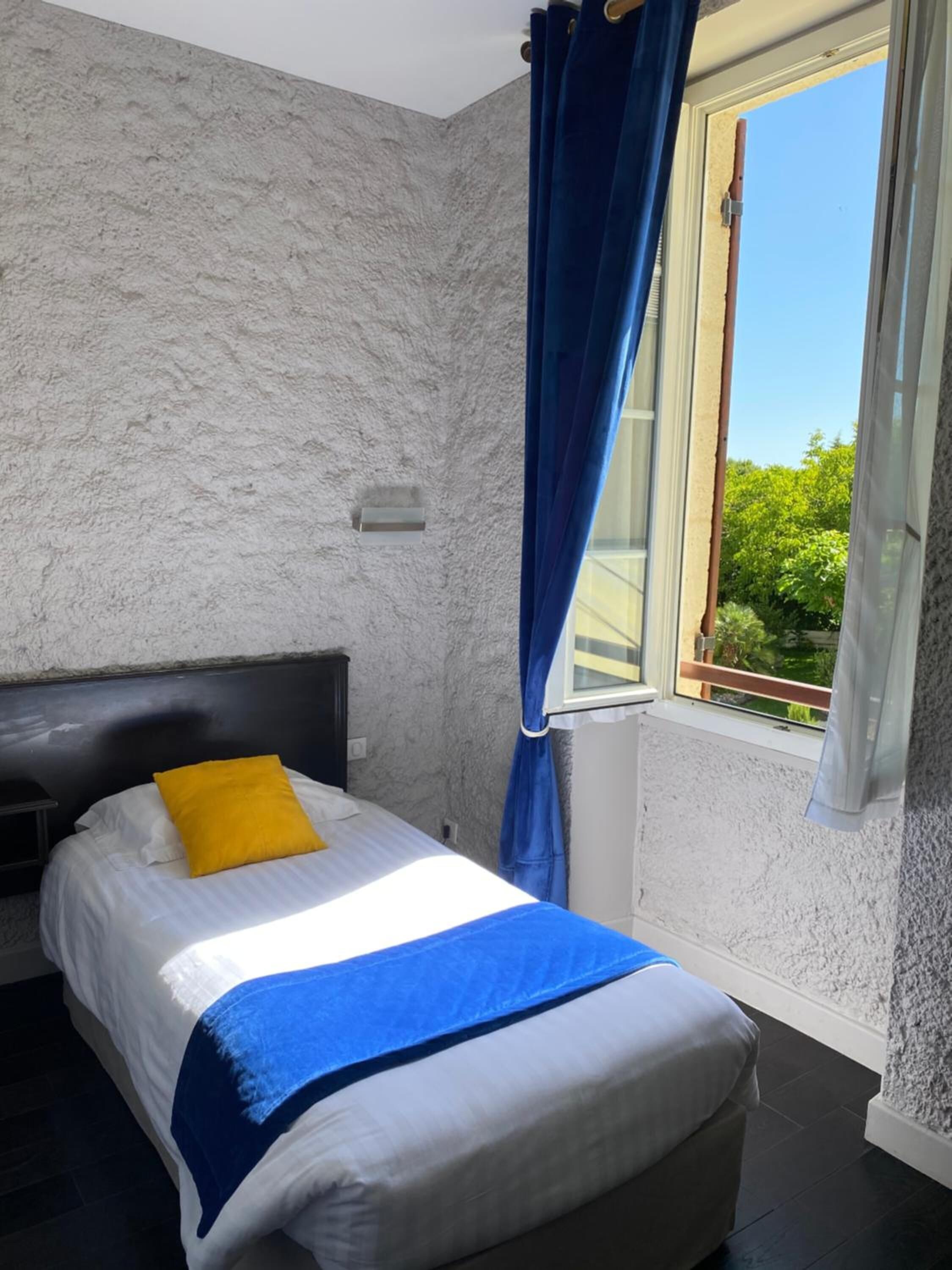 Un dormitorio con una cama, una ventana con cortinas azules y vistas a la vegetación.