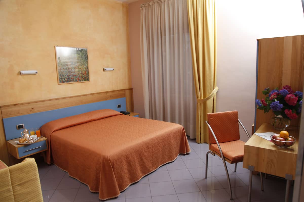 Une chambre d’hôtel avec un lit, un bureau, une chaise, une table de chevet et un tableau au mur.