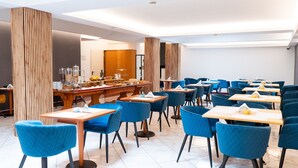 A modern dining area with blue upholstered chairs and wooden tables, featuring a buffet setup and a separate dining section. - Diana Pompei (Pompei)