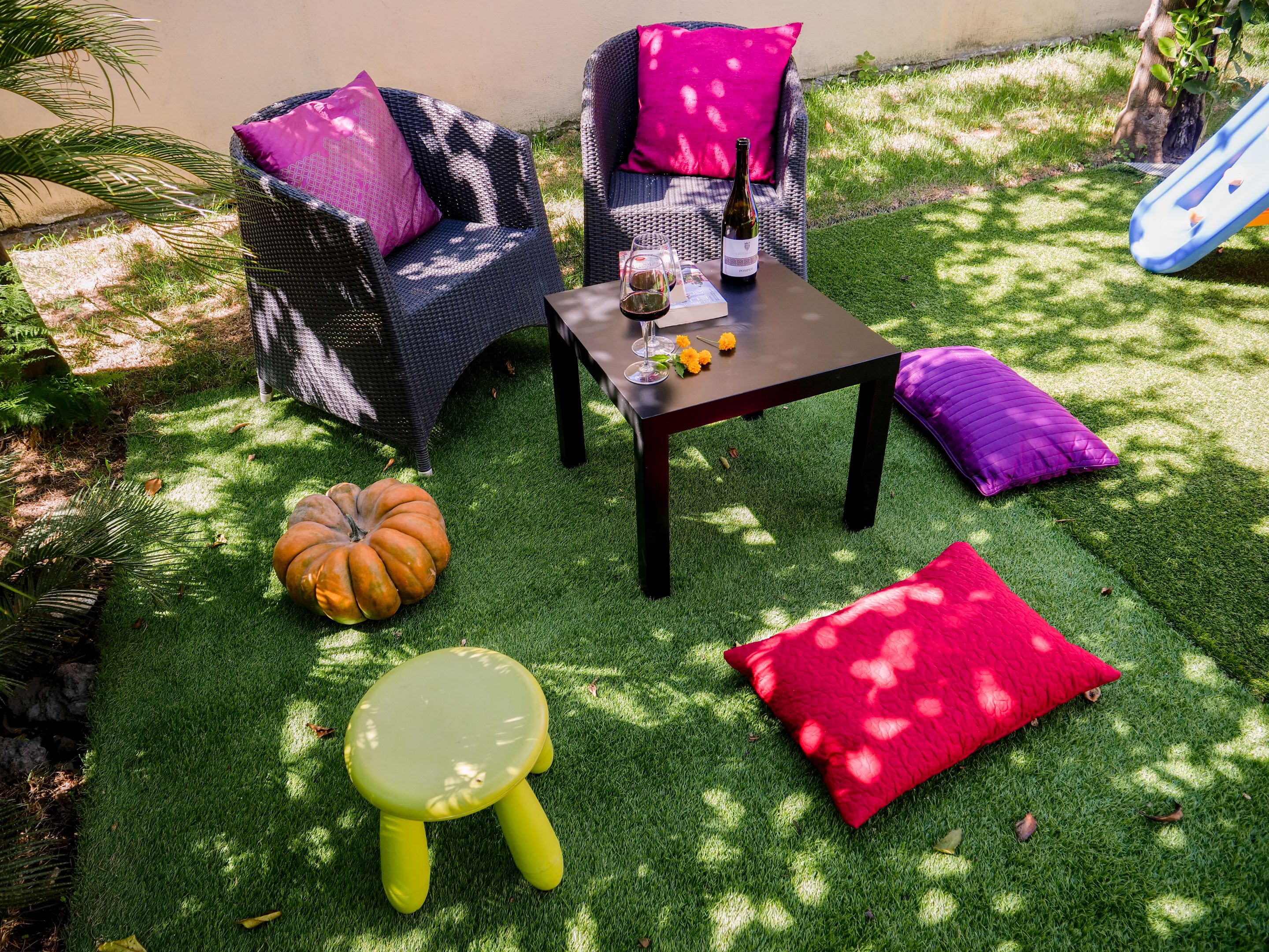 A patio with wicker furniture, a table with a bottle, a pumpkin, and a small stool.