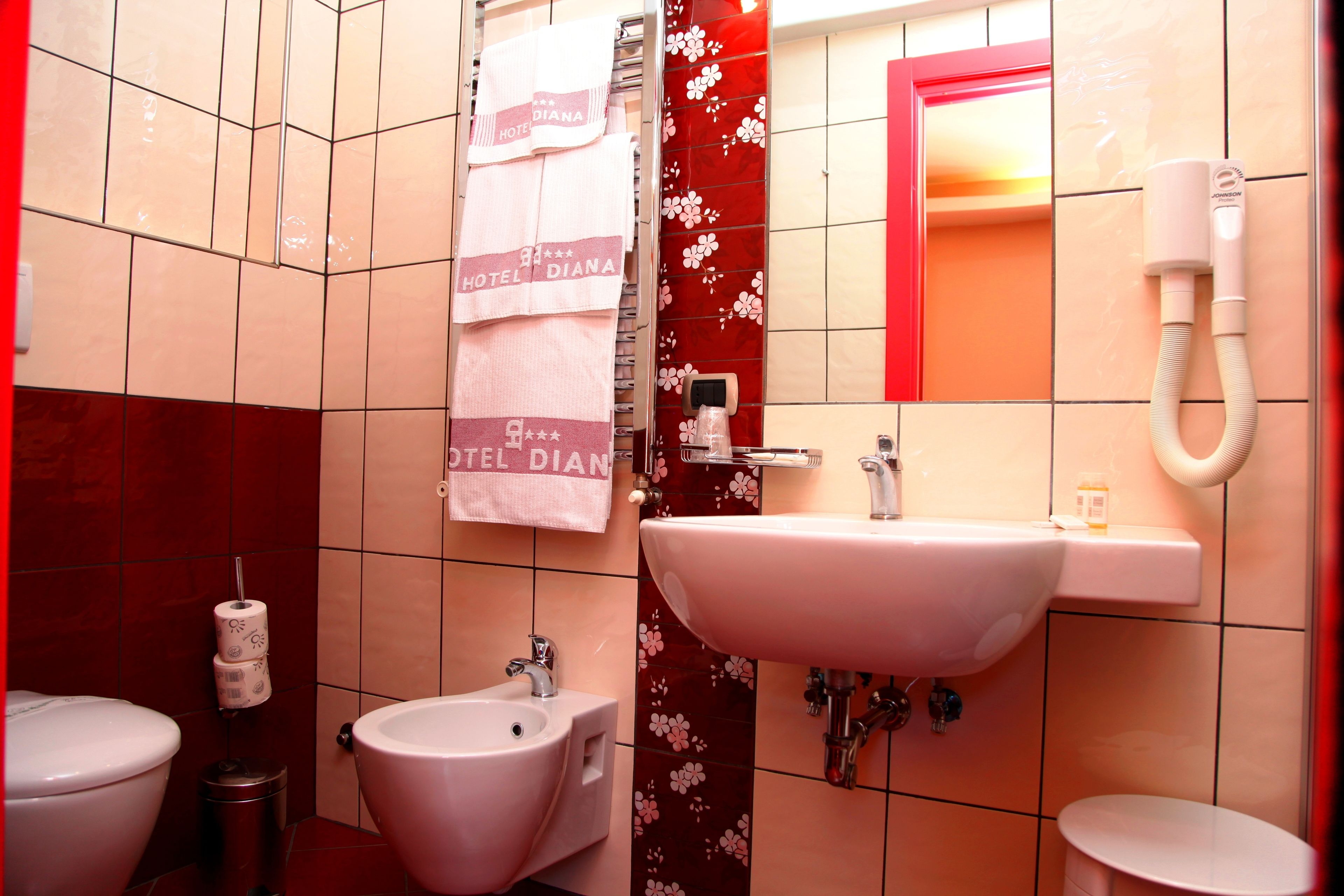 Un baño con lavamanos, bidé, inodoro y un perchero con toallas.
