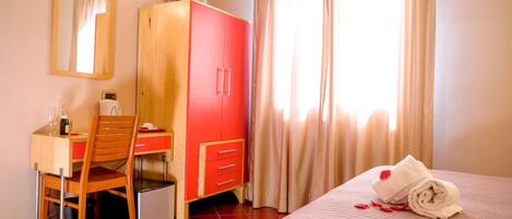 Habitación de hotel con cama, escritorio con silla, armario, televisor en la pared y ventana con cortinas.