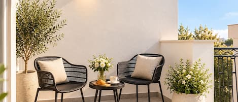 Een balkon met twee rieten stoelen, een kleine ronde tafel met een bloevas en potplanten.