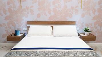A neatly made bed with a wooden headboard, two bedside tables with a phone and a vase of flowers, and a patterned bedspread.