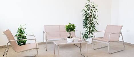 Una habitación con un sofá, dos sillas, una mesita y tres plantas en macetas.
