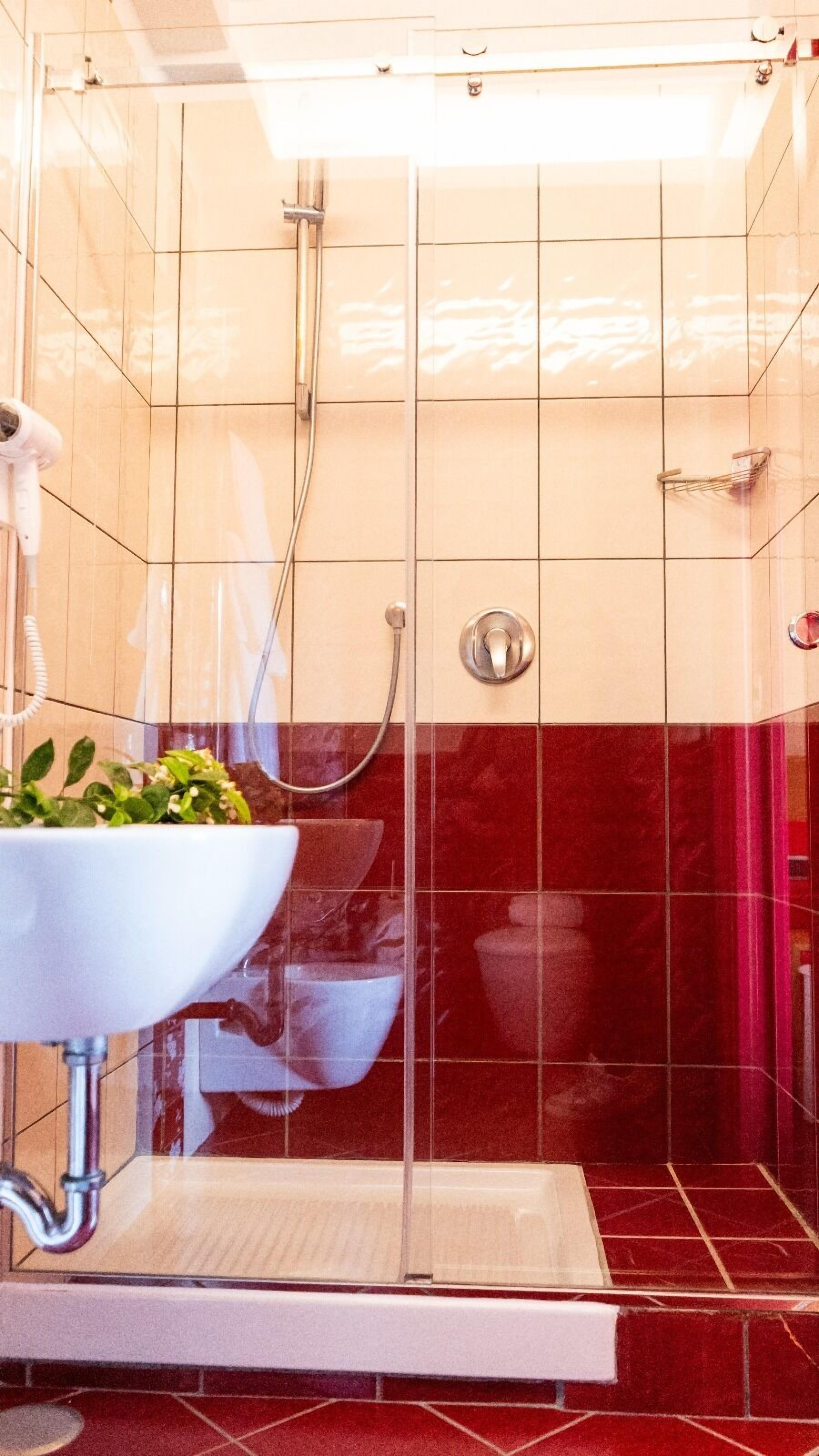 Un baño con un lavabo blanco, ducha y paredes con azulejos rojos.