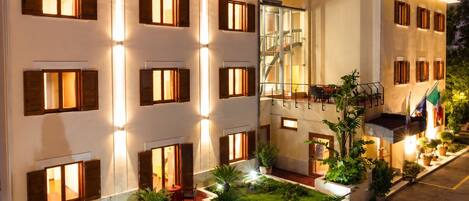 A hotel with multiple balconies, a central staircase, and a well-maintained garden.
