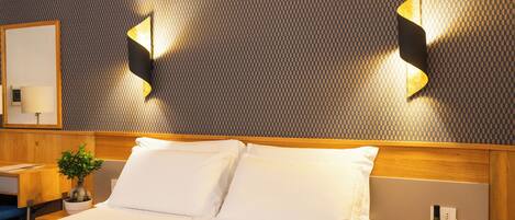 Une chambre d’hôtel avec un lit, une table de chevet avec une lampe, une plante en pot et un luminaire fixé au mur.