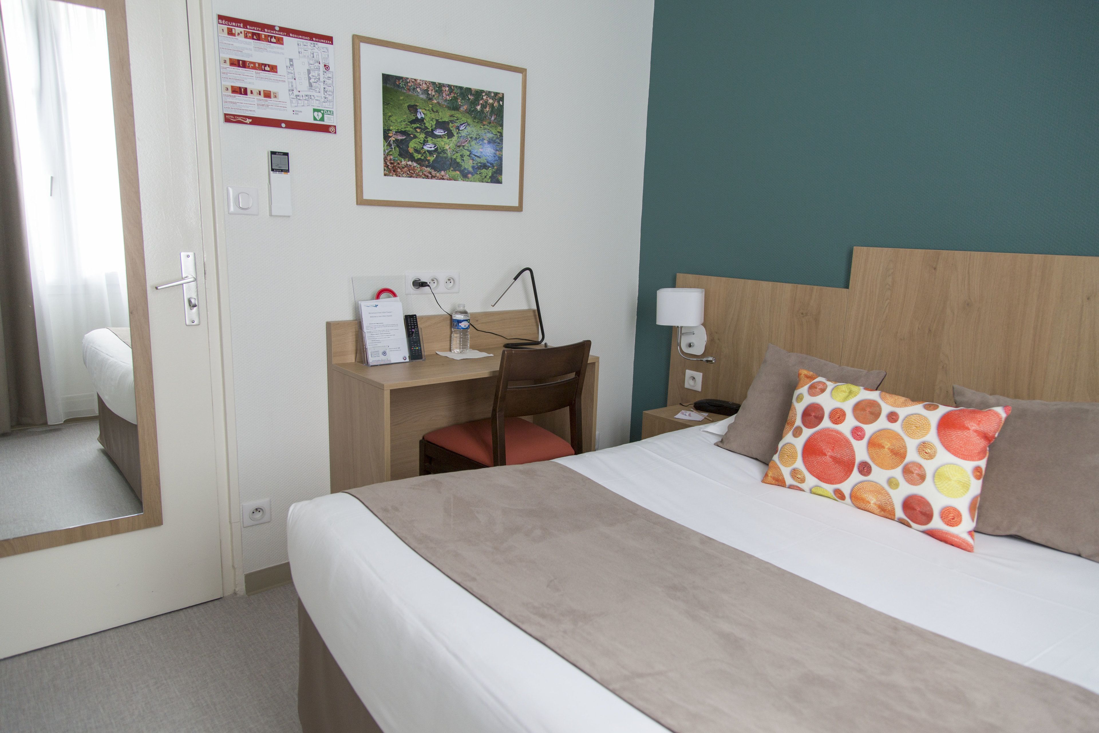 Una habitación de hotel con cama, escritorio y silla, lámpara, mesita de noche y teléfono instalado en la pared.
