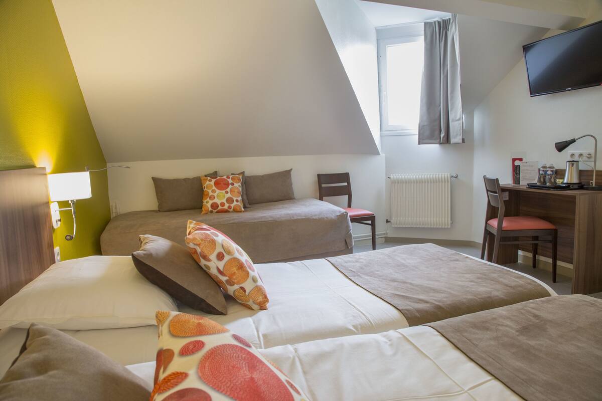 A hotel room with two beds, a desk, a chair, a TV, and a window with curtains.