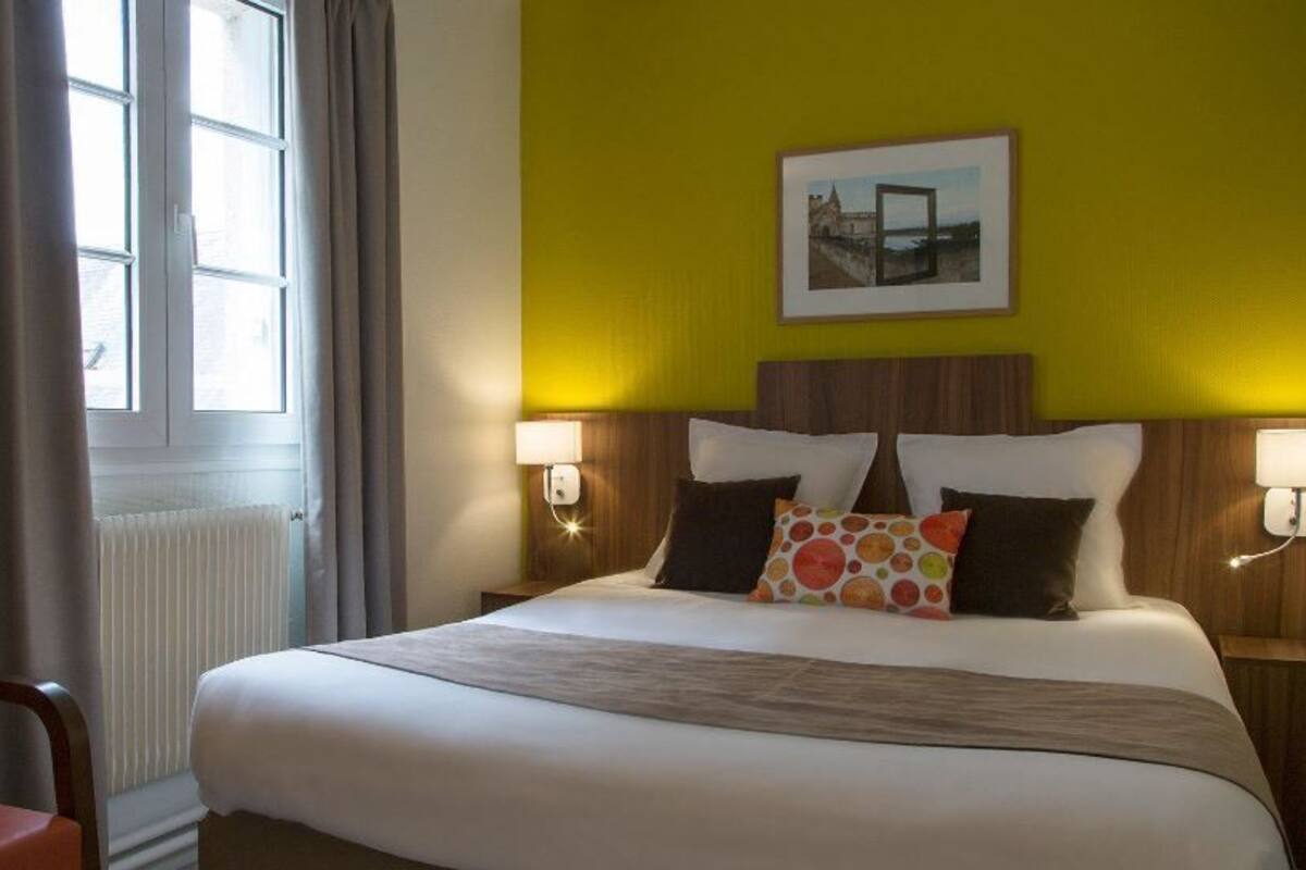 A hotel room with a bed, two bedside lamps, a chair, and a window with curtains.