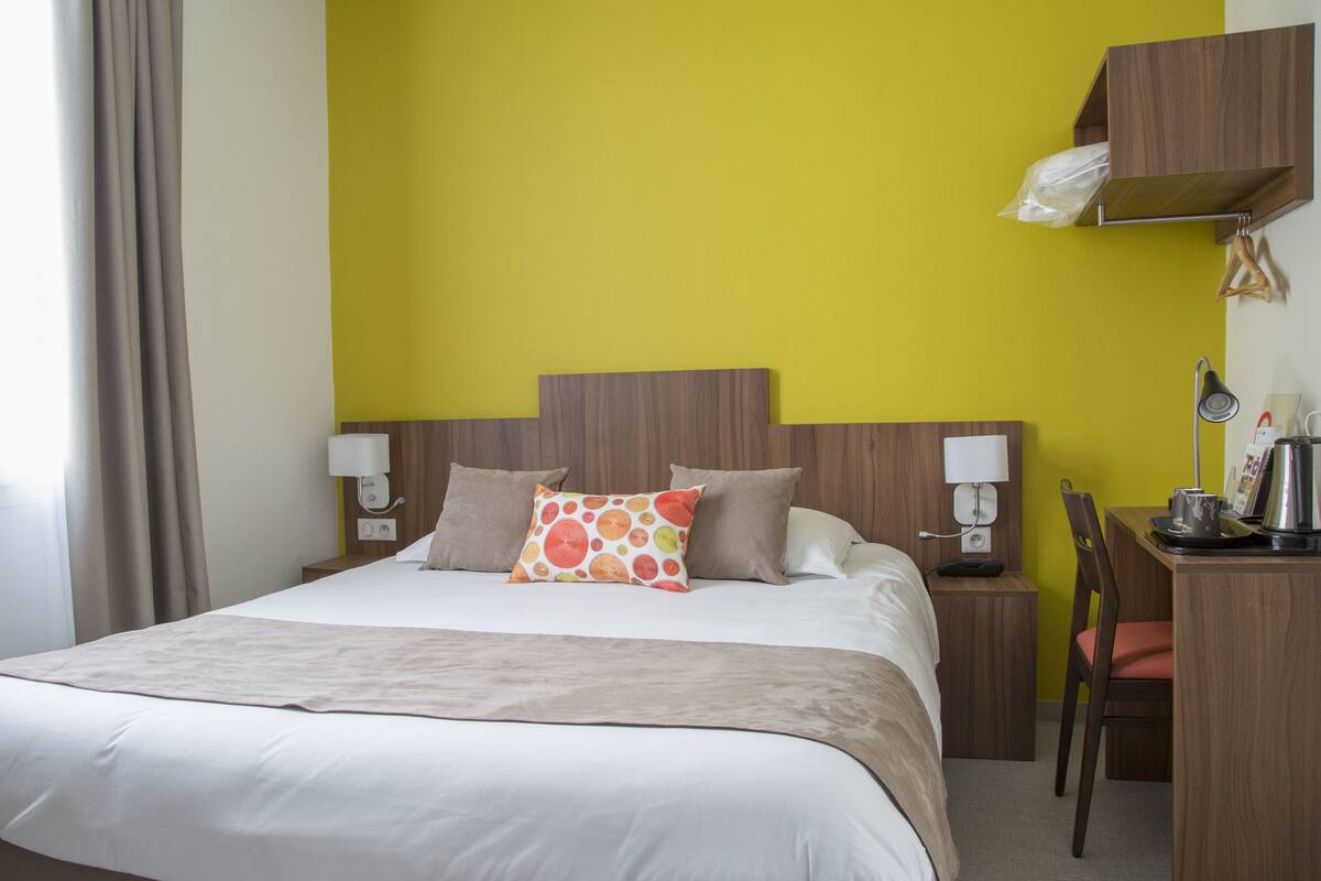A hotel room with a bed, bedside tables, a desk, and a chair.