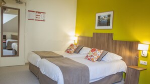 Habitación de hotel con dos camas, un cabecero de madera y una mesita de noche pequeña con una lámpara.