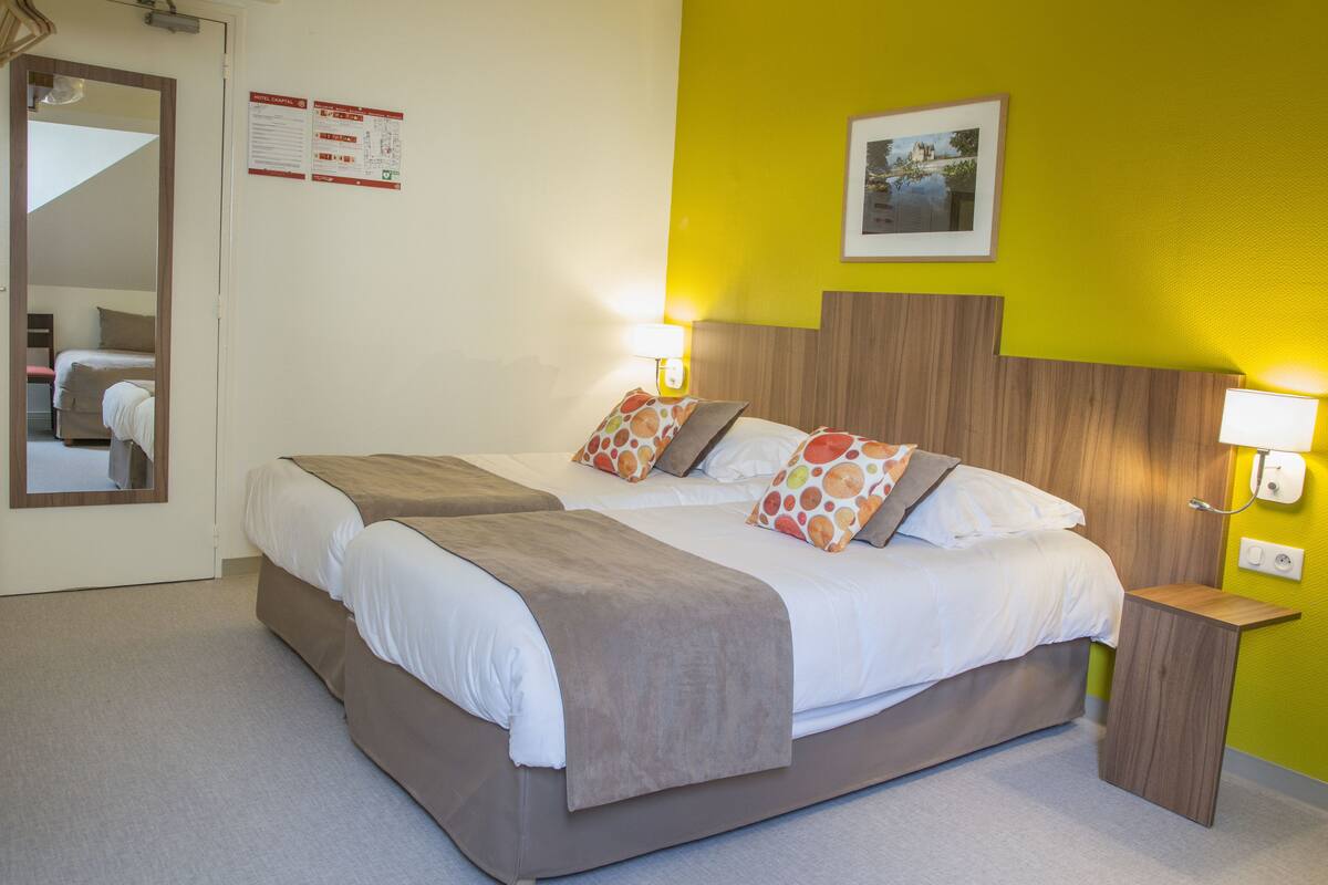 A hotel room with two beds, a wooden headboard, and a small bedside table with a lamp.