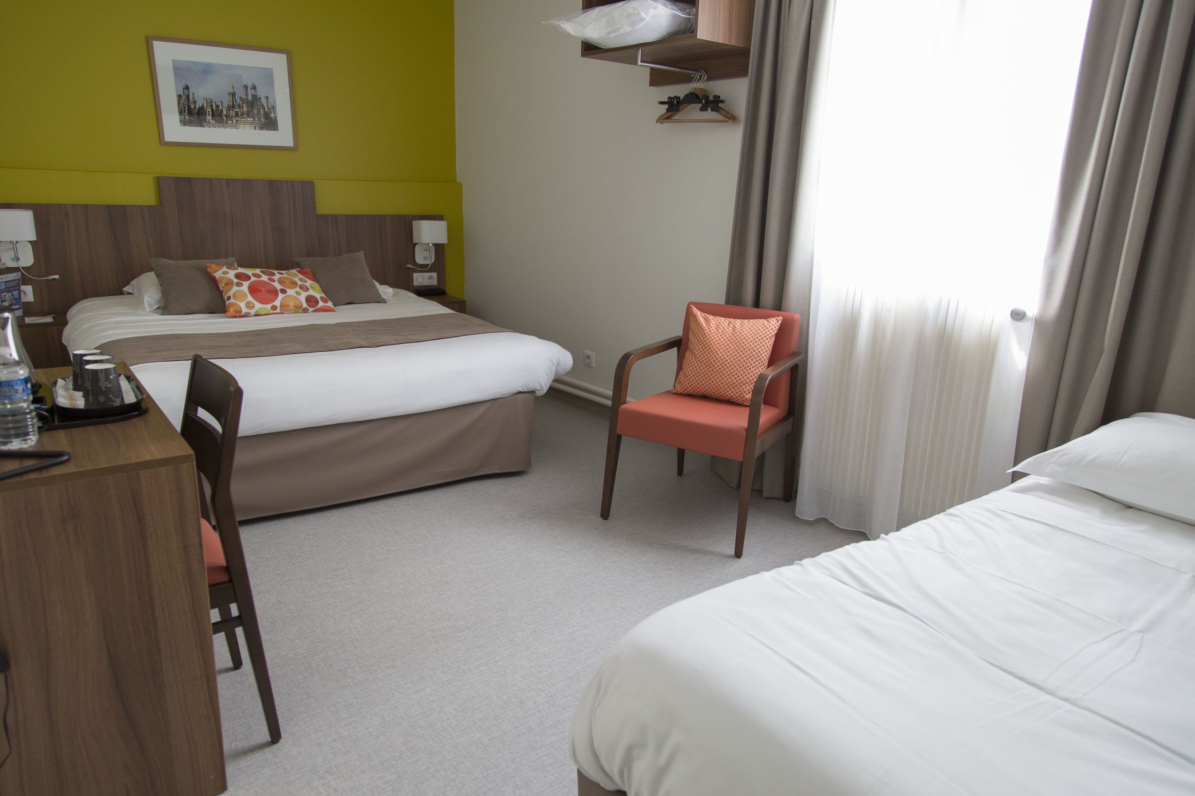 A hotel room with a bed, a desk, a chair, and a window with curtains.