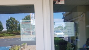 A view through a glass door of a building with outdoor seating and a parking lot.