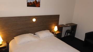 Ein Hotelzimmer mit einem Bett, zwei Nachttischlampen, einem Schreibtisch mit Stuhl und einem gerahmten Bild an der Wand.