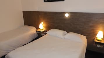 Una habitación de hotel con dos camas individuales, cada una con una mesita de noche y una lámpara. Encima de las camas hay un cuadro colgado en la pared.