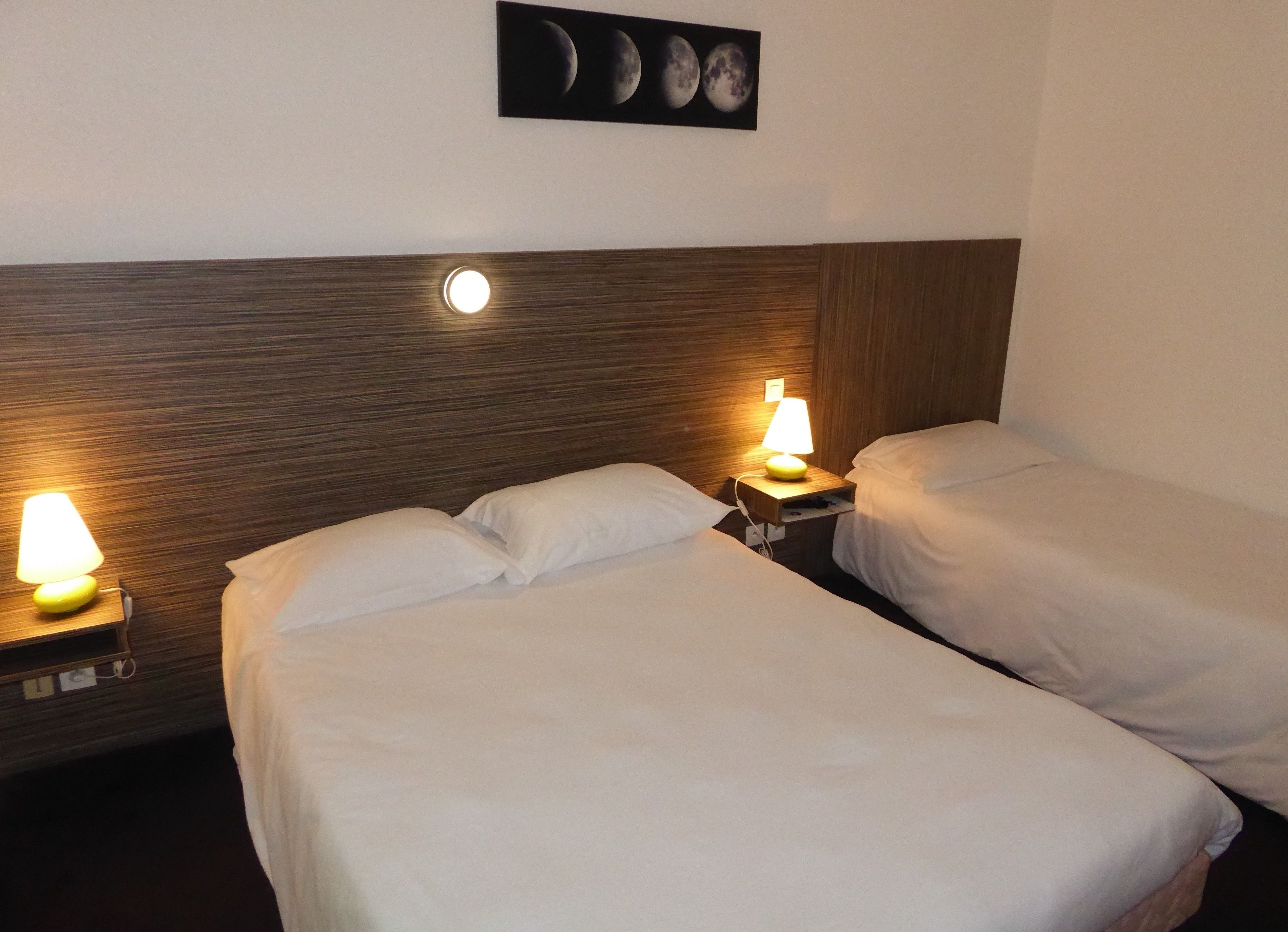 Habitación de hotel con dos camas individuales, cada una con mesita de noche y lámpara. Encima de las camas, hay un cuadro colgado en la pared.