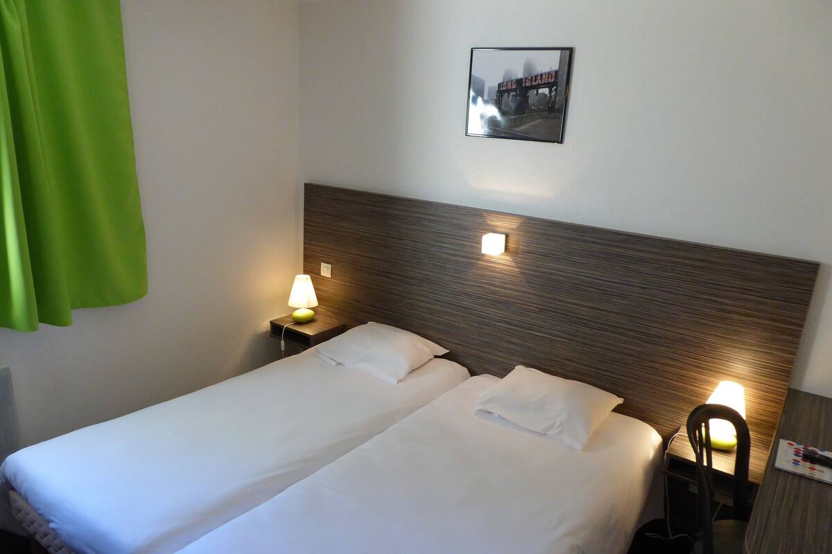 A hotel room with a double bed, two bedside tables with lamps, a green curtain, and a framed picture on the wall.