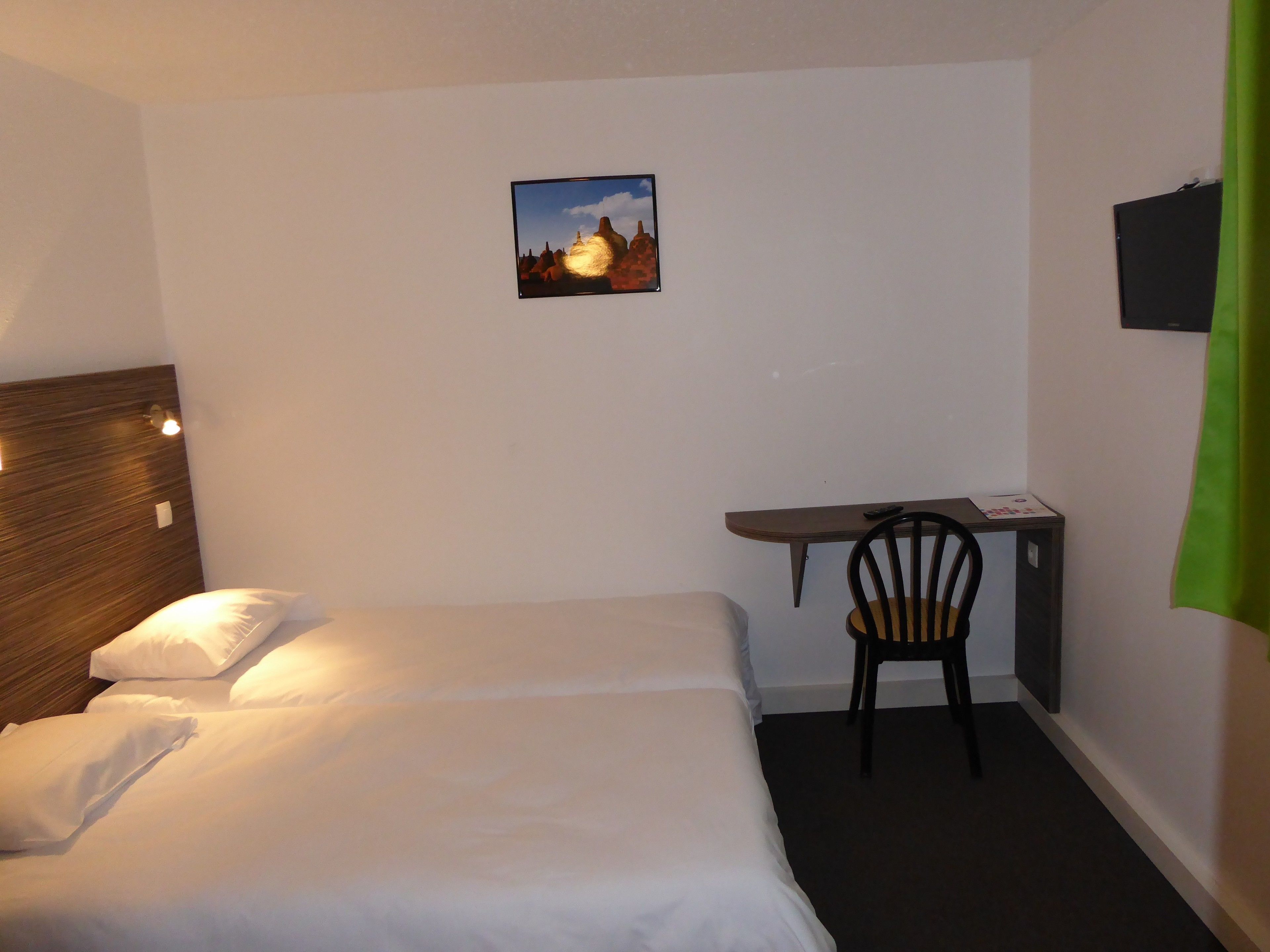 Une chambre d’hôtel avec un lit, un bureau, une chaise, une télévision et un tableau au mur.