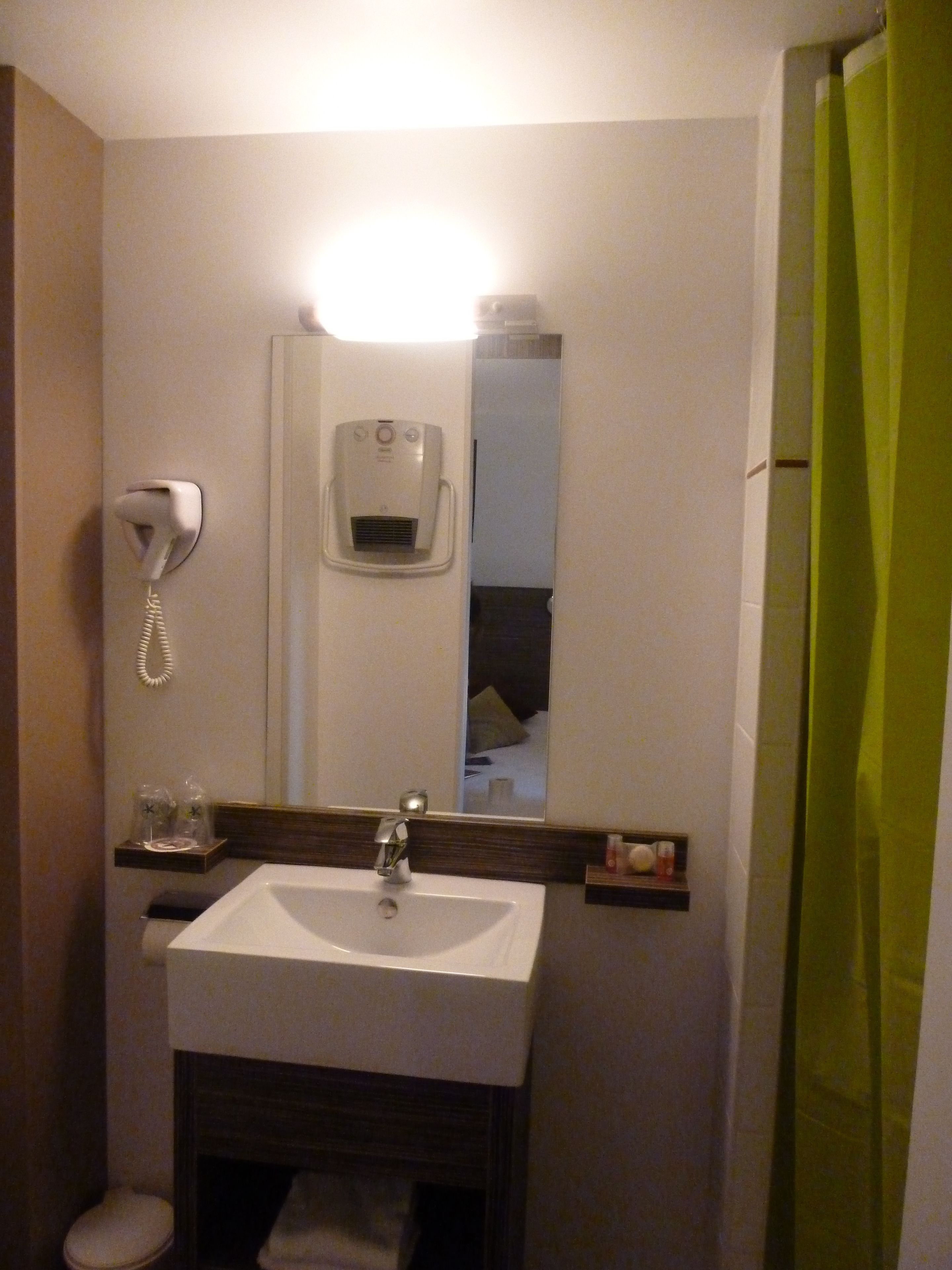 A bathroom with a white sink, a mirror, a hand dryer, and a telephone.