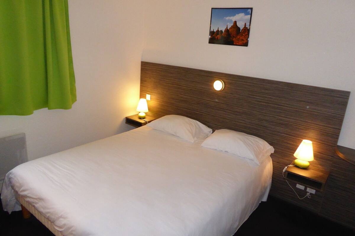 A hotel room with a bed, two bedside tables with lamps, a picture on the wall, and a green curtain.