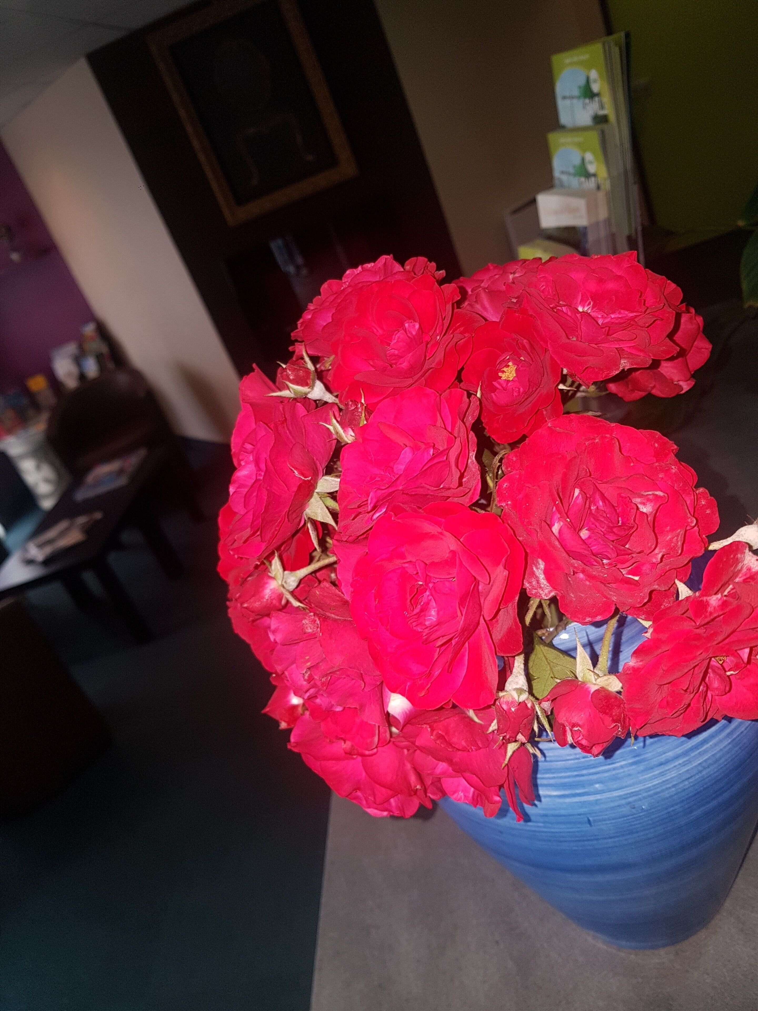 Un ramo de flores rojas en un jarrón azul sobre una mesa.