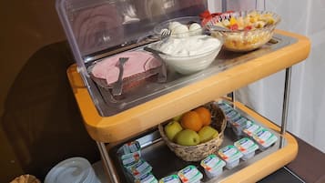 A buffet setup with a variety of food items including a bowl of fruit, a container of yogurt, and a tray of sliced ham.