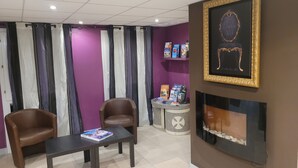 A room with two brown leather chairs, a dark wooden table, a purple wall, a fireplace with white stones, and a framed artwork above it.