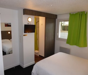 A hotel room with a bed, a television, a bathroom with a shower, and a window with green curtains. - Hôtel Le Cosy Blois Nord (Villebarou)