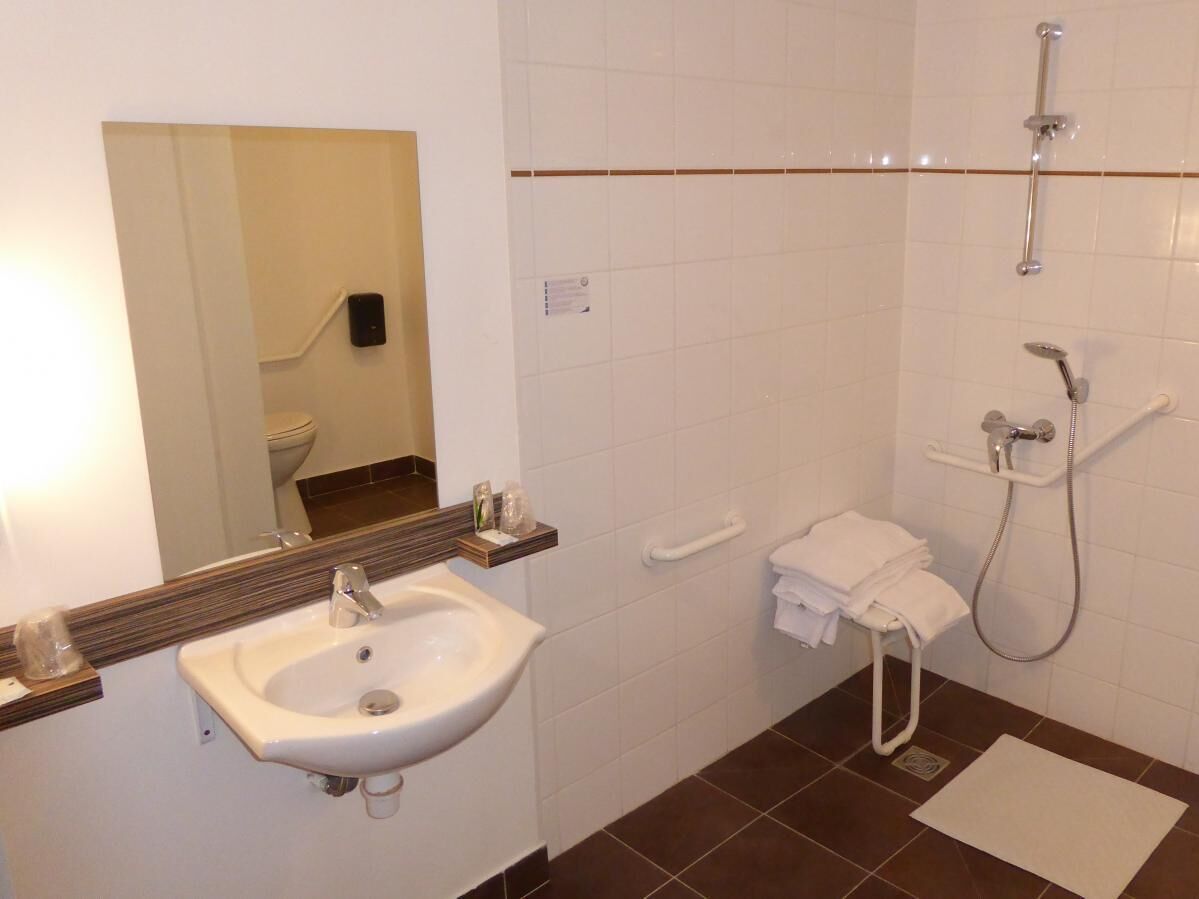 A bathroom with a sink, mirror, towel rack, shower, and a toilet.