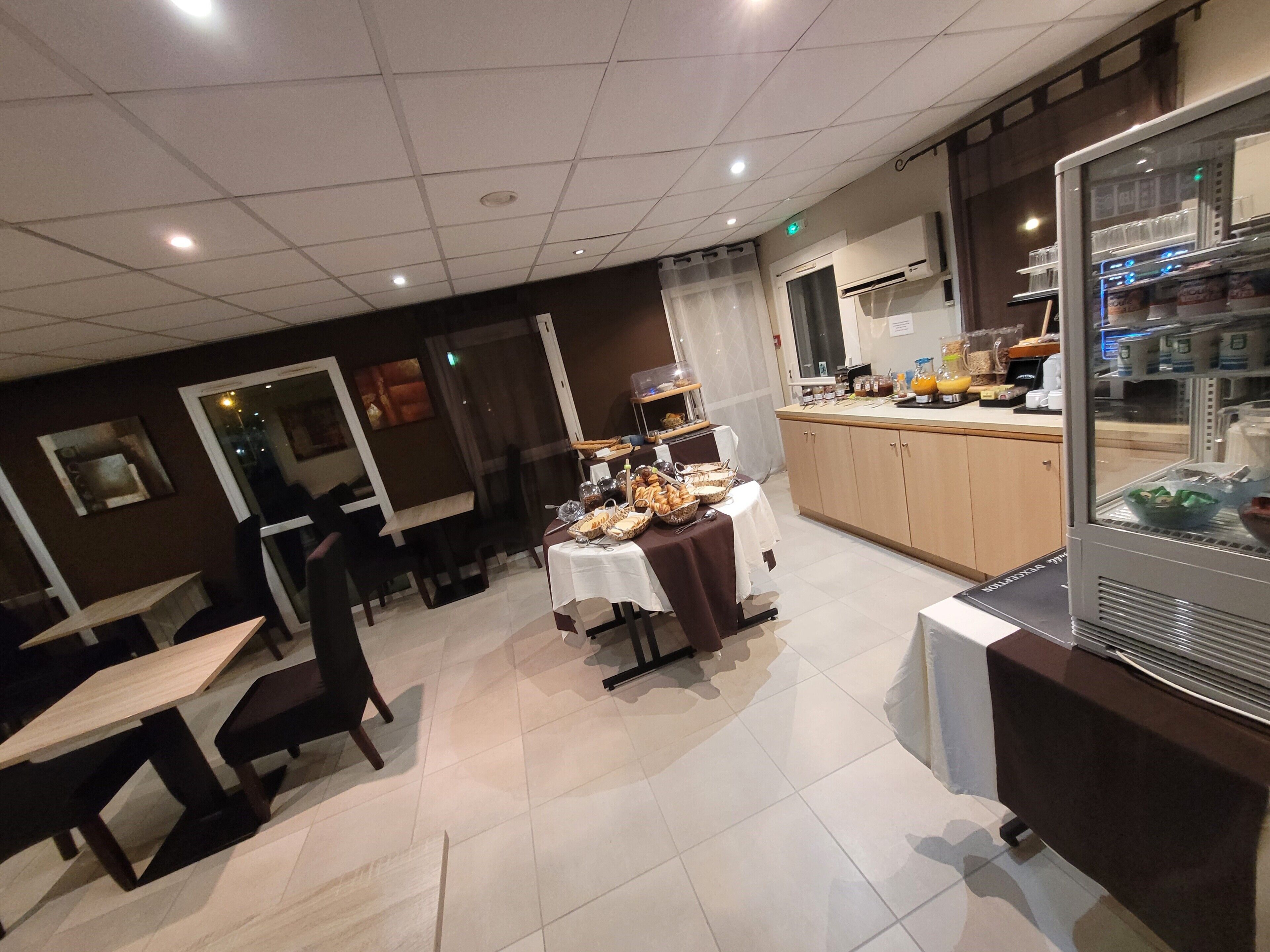 Un espace repas avec des tables et des chaises, un buffet proposant divers plats et un réfrigérateur rempli de boissons.
