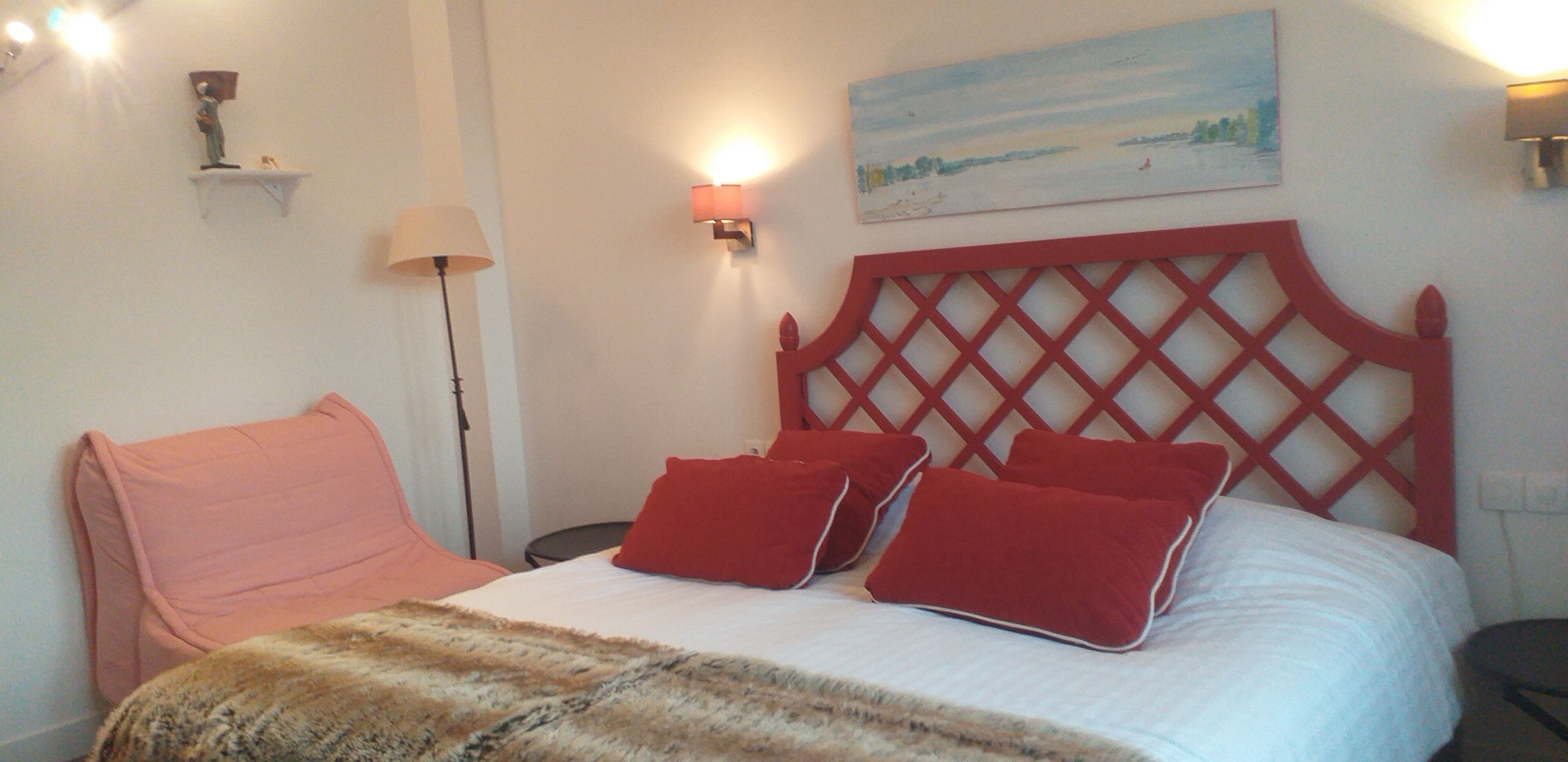 A bed with a red headboard, a pink chair, and a lamp.