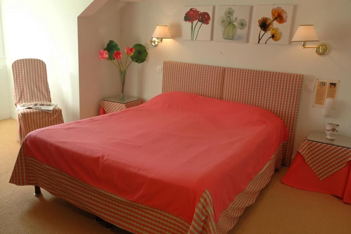 A bedroom with a large bed, a chair, a nightstand, and wall-mounted lamps.