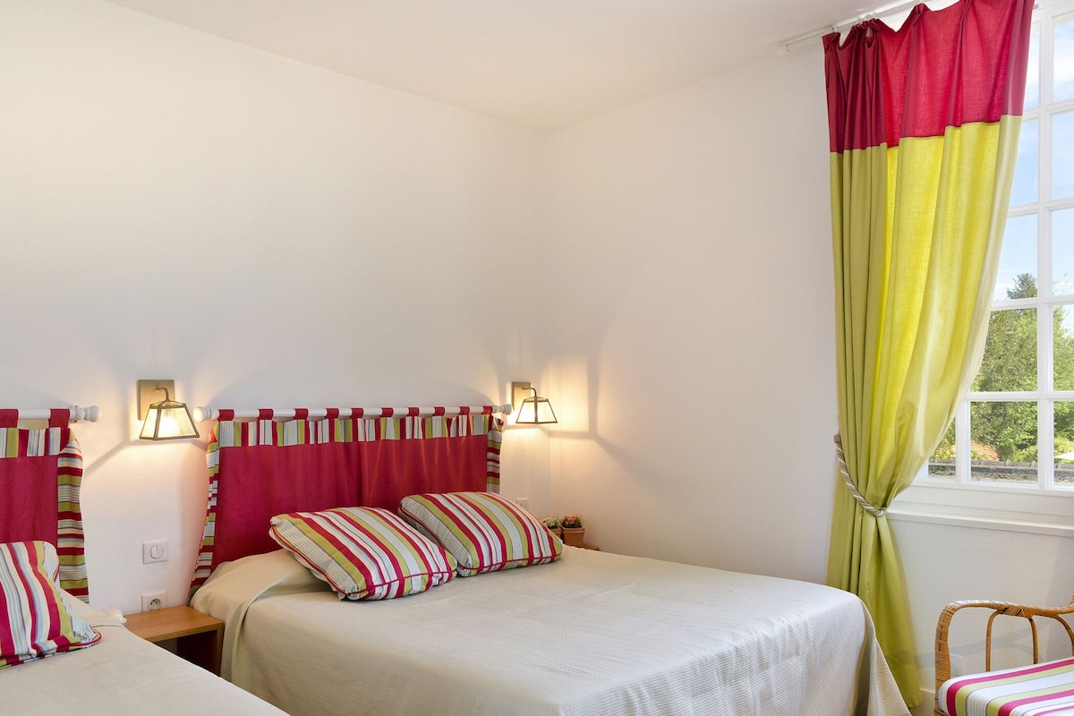 Un dormitorio con dos camas, almohadas a rayas y un ventanal con cortinas.
