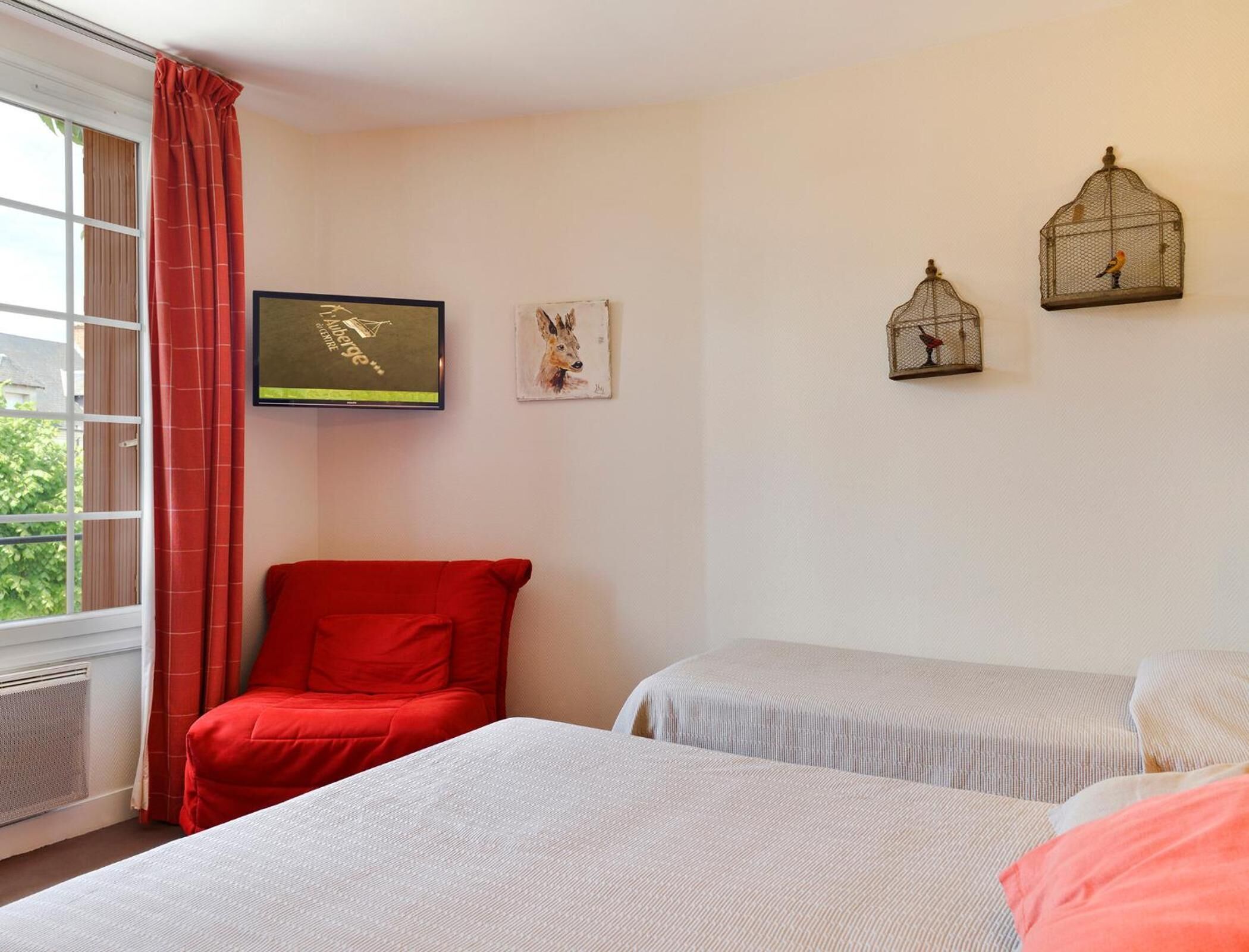 A bedroom with two beds, a red chair, a television, and wall-mounted birdcages.
