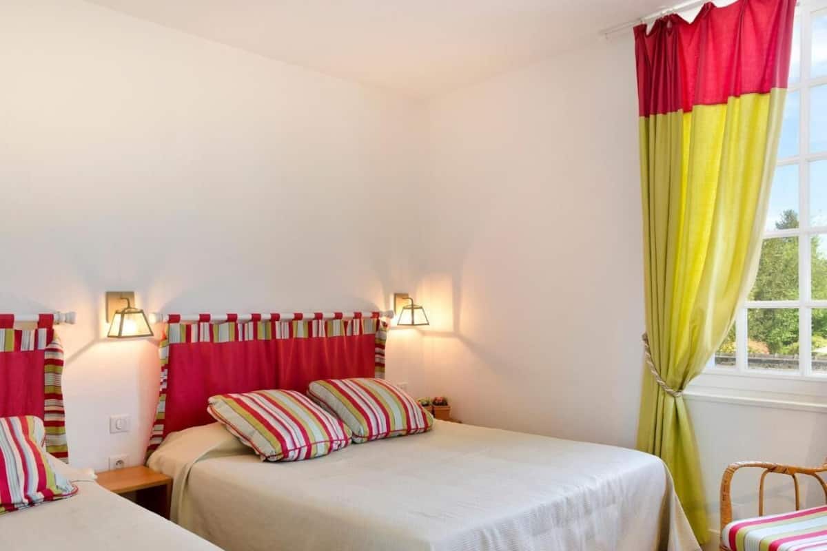 Una habitación con dos camas, cada una con almohadas a rayas, una ventana con cortinas amarillas y lámparas fijadas a la pared.