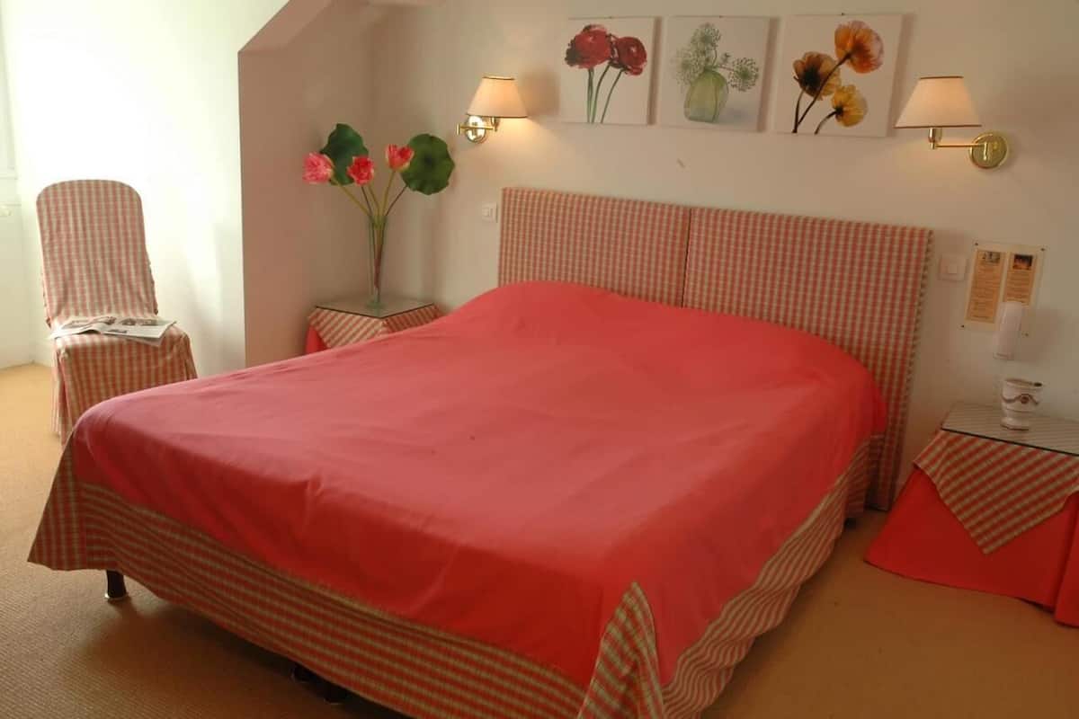 Un dormitorio con una cama grande, una silla, una mesita de noche y lámparas fijadas a la pared.