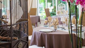 A dining area with wicker furniture, a table set with plates and napkins, and a birdcage. - LOGIS Auberge du Centre (Chitenay)