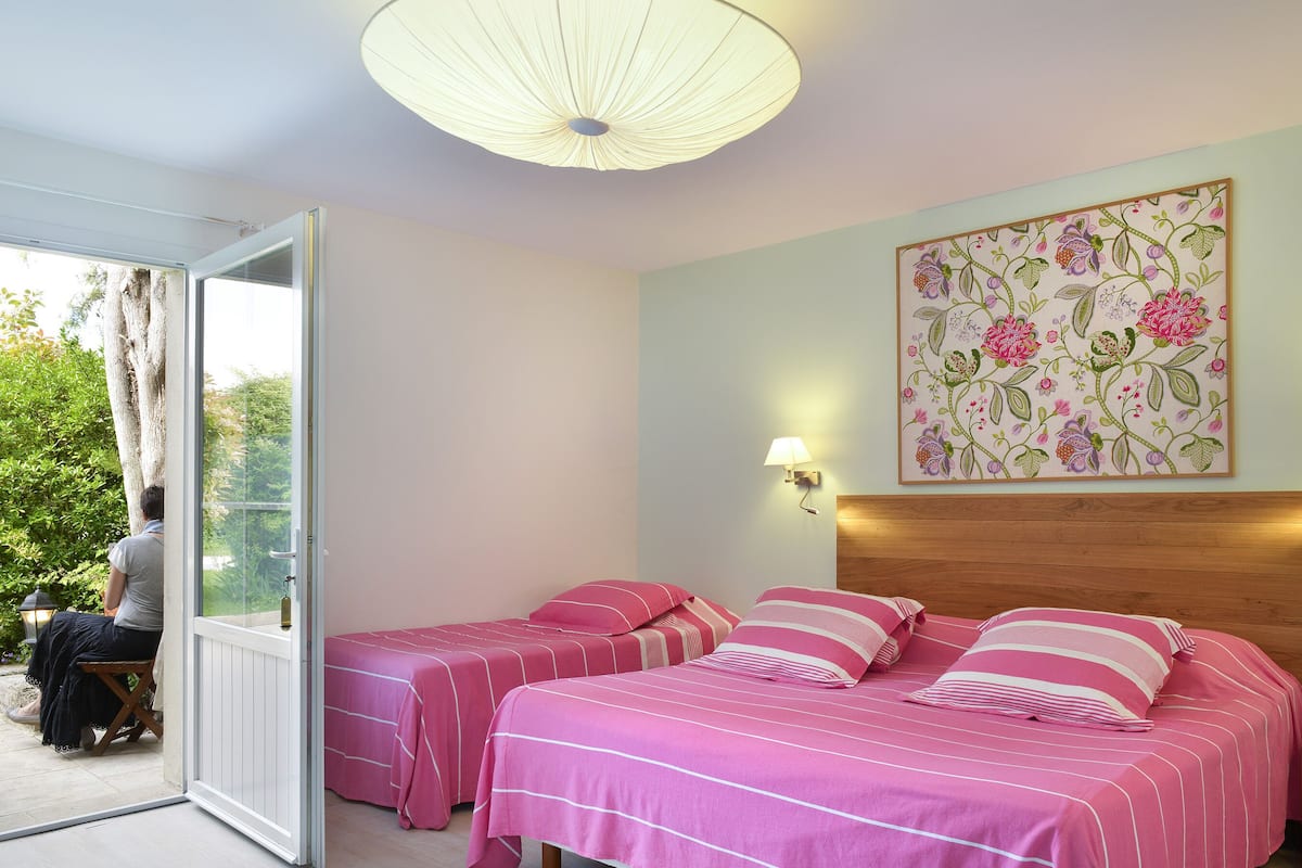 Un dormitorio con dos camas, cabeceros de madera, una decoración floral en la pared y vistas a la vegetación a través de una puerta de cristal.