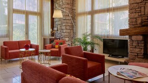 A living room with red sofas, a TV, and a stone wall. - Hotel Ariston (Malcesine)