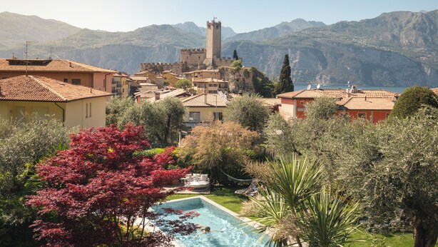 A villa with a swimming pool, surrounded by lush greenery and a mountain backdrop. - Hotel Ariston (Malcesine)