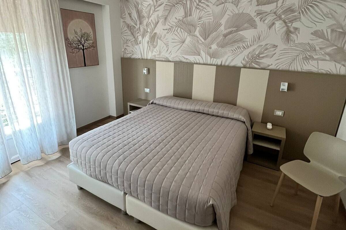 A bedroom with a bed, a nightstand, a chair, and a wall with a leaf pattern.