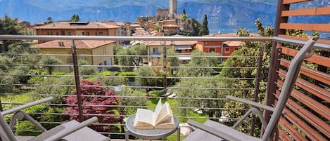 A balcony with two chairs and a table, overlooking a town with a castle and mountains.