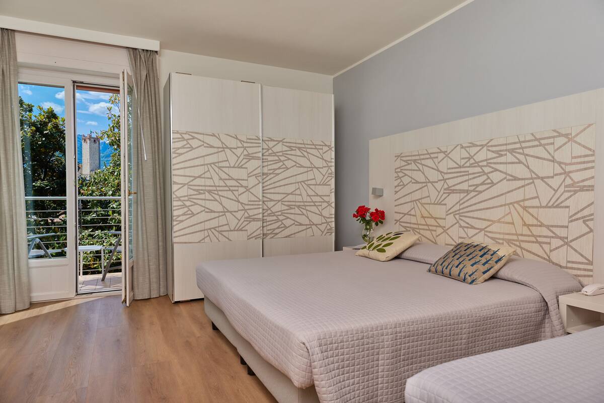 A bedroom with two beds, a sliding door to a balcony, and a geometric wall design.