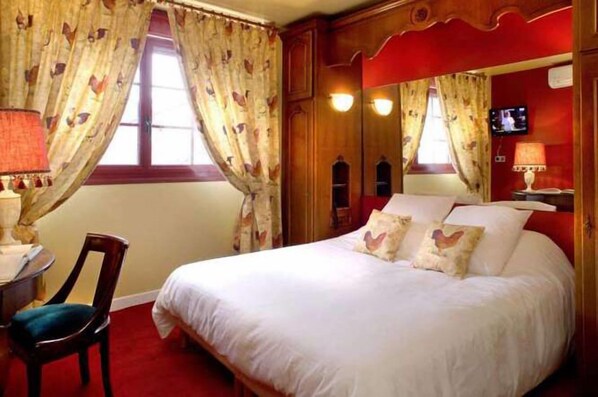 A hotel room with a large bed, a wooden headboard, a desk with a chair, and a television on the wall.