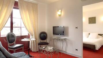 Une chambre d’hôtel avec un tapis rouge, un lit, une télévision, une petite table, une chaise et une fenêtre avec des rideaux.