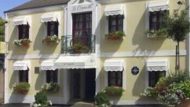 A two-story building with a white facade, multiple windows with white shutters, and a balcony with potted plants. - Hôtel de la Cognette (Issoudun)